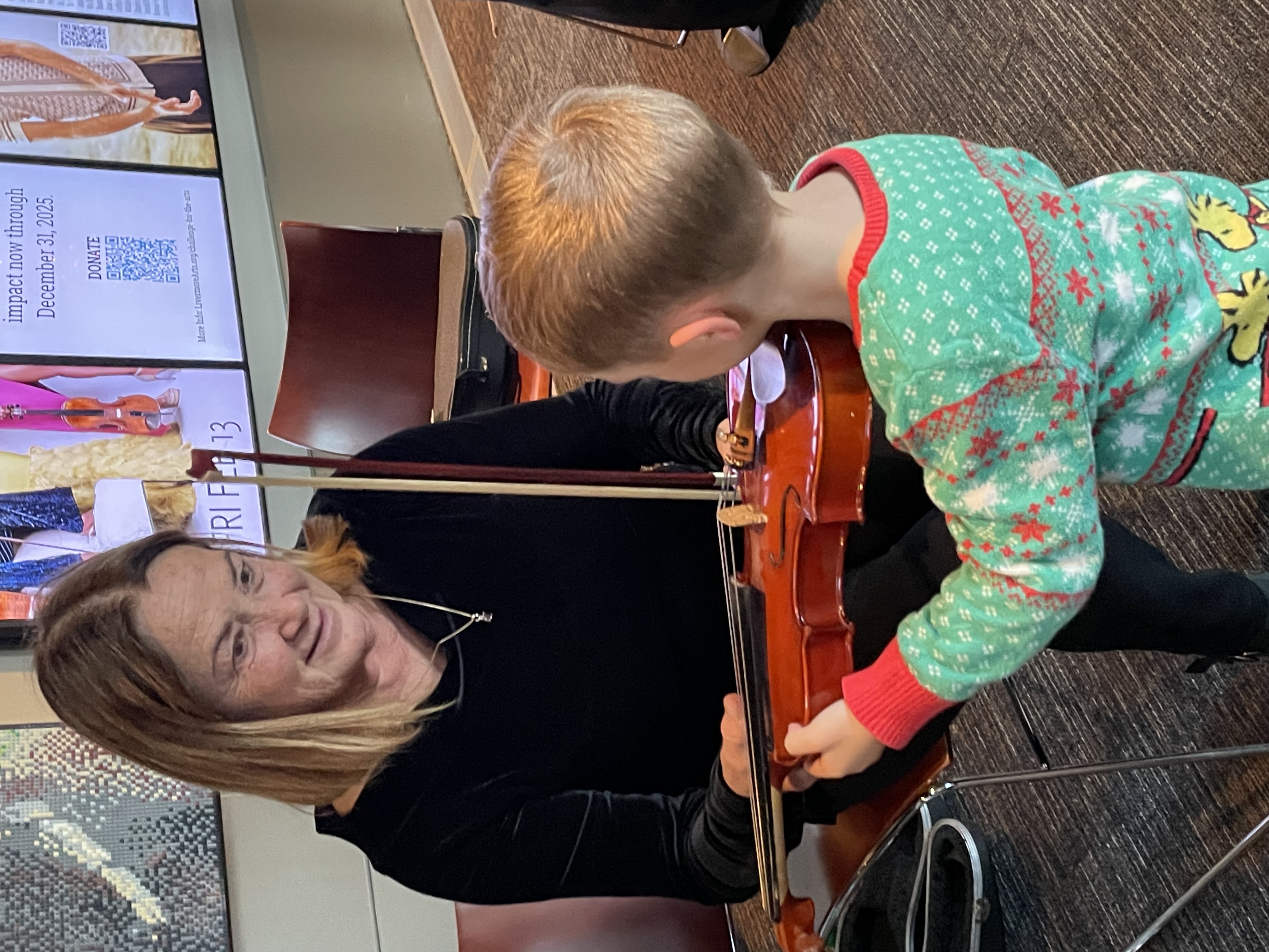 child meets violin, helped by LAS player Sue Ivie